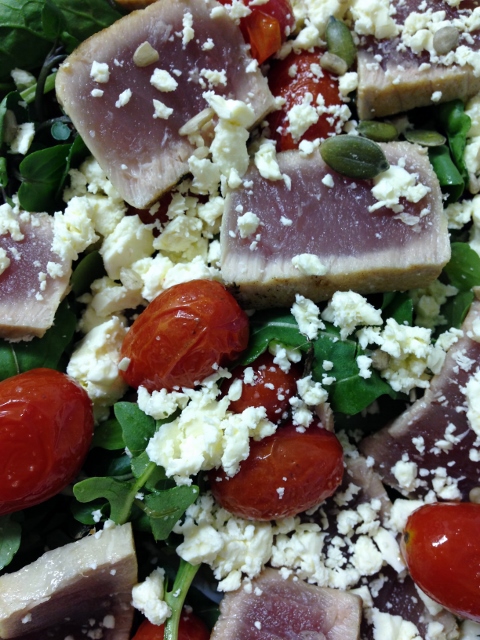 Seared tuna pieces with feta and cooked baby tomato's in a green salad